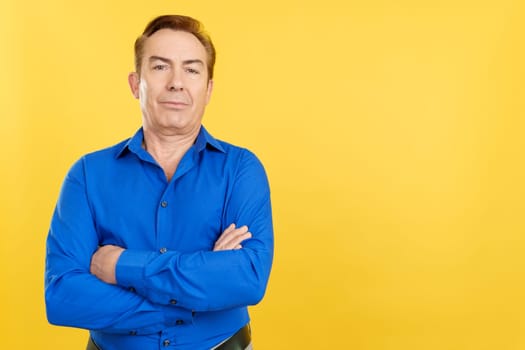 Mature man standing and looking at the camera with arms crossed in studio with yellow background