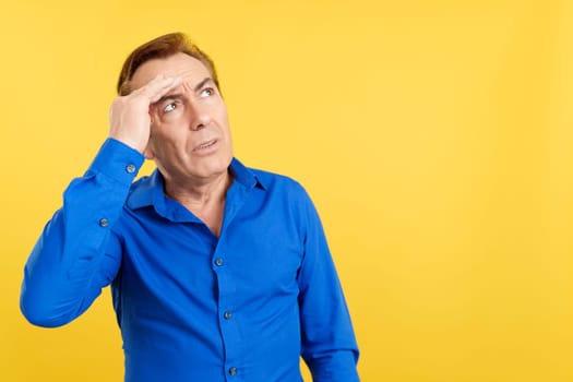 Mature man gesturing that he is forgetting something in studio with yellow background