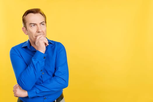 Mature man gesturing pensive that he is forgetting something in studio with yellow background