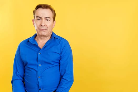 Mature man looking at camera with sad expression in studio with yellow background