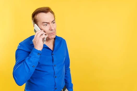 Angry mature man talking to the mobile in studio with yellow background