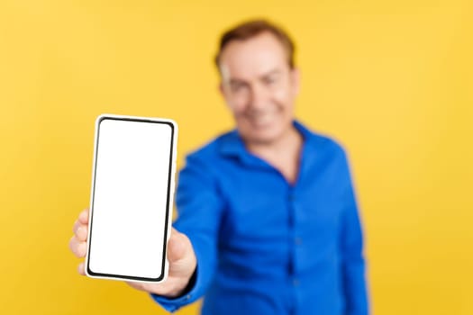 Blank screen of the mobile held by an mature man in studio with yellow background