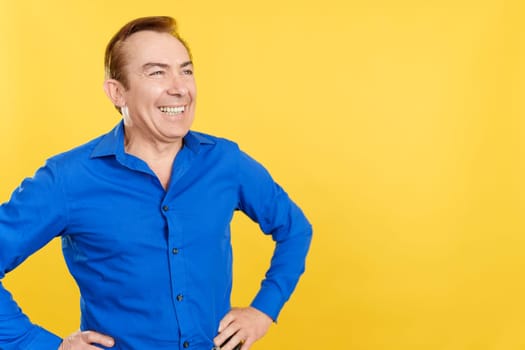 Smiley mature man standing with the hands on the hips in studio with yellow background