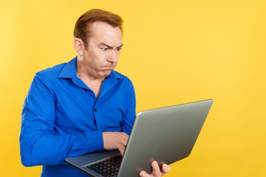 Mature man standing with a problem with a laptop in studio with yellow background
