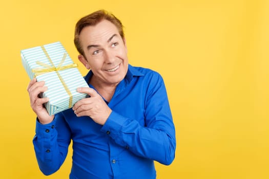 Curious mature man receiving a Father's Day gift in studio with yellow background