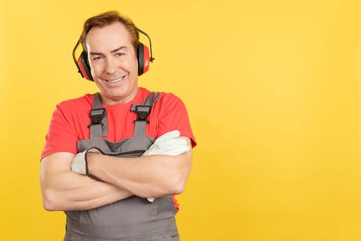 Smiley mature man carpentry worker looking at camera in work uniform in studio with yellow background