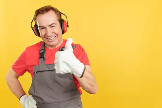 Smiley mature worker gesturing approval in work uniform in studio with yellow background