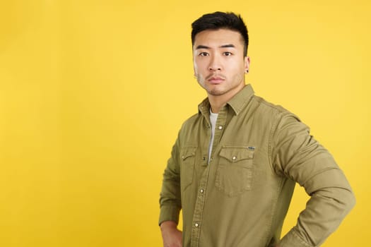 Confident and serious chinese man standing looking at the camera in studio with yellow background