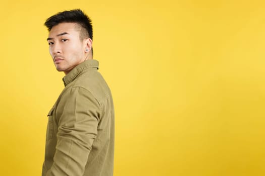 Serious chinese man turning to look at the camera in studio with yellow background