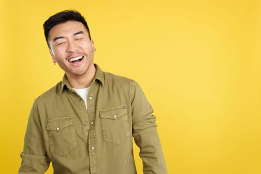 Chinese man laughing with eyes closed while standing in studio with yellow background