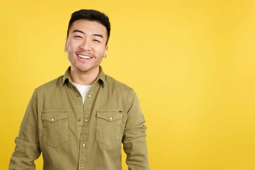 Happy chinese man smiling at the camera in studio with yellow background