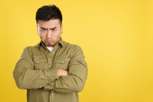 Chinese man crossing the arms with an angry expression while looking at camera in studio with yellow background