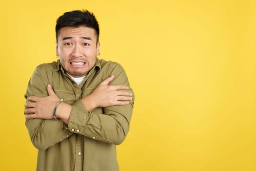 Chinese man looking at camera in the cold in studio with yellow background