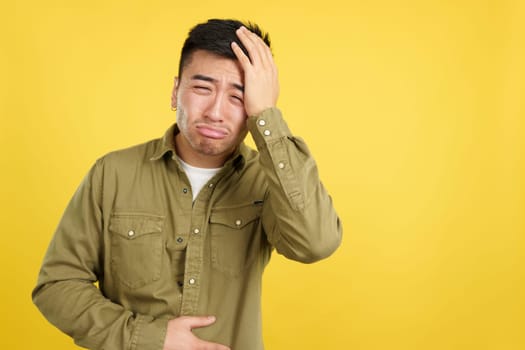 Chinese man gesturing bodily discomfort and headache in studio with yellow background