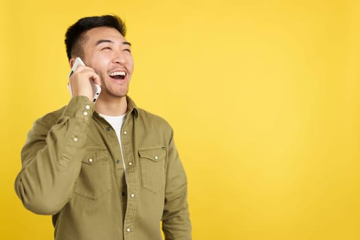 Happy chinese man talking to the mobile in studio with yellow background