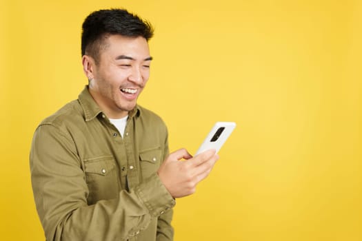 Happy chinese man smiling while using the mobile in studio with yellow background