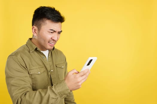 Chinese man gesturing worried while using a mobile in studio with yellow background