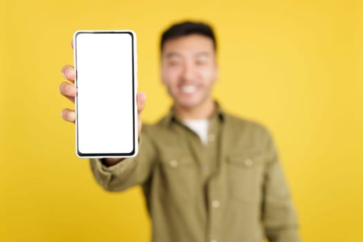 Focus on a blank screen of the mobile held by a chinese man in studio with yellow background