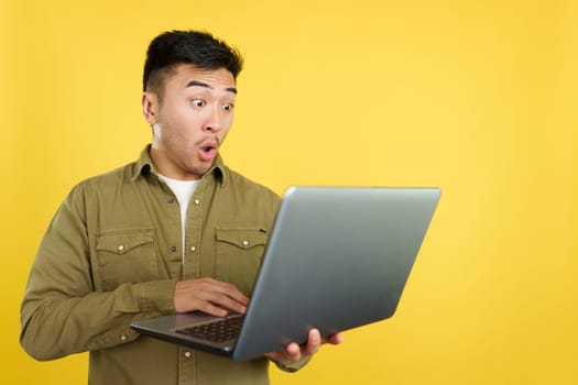 Chinese man with a surprised look using a laptop in studio with yellow background