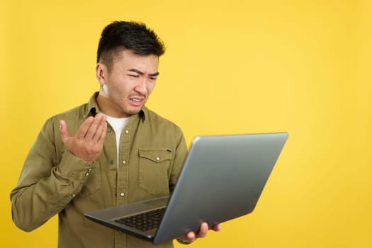 Chinese man having a problem with a laptop in studio with yellow background