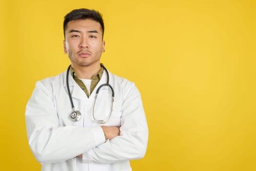 Serious chinese doctor looking at the camera with arms crossed in studio with yellow background