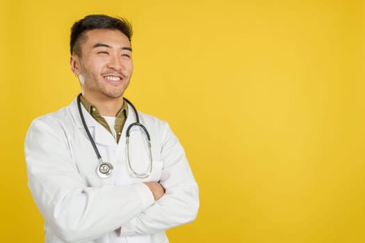 Friendly chinese doctor in uniform and stethoscope in studio with yellow background