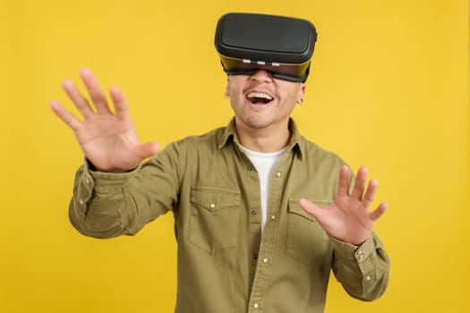 Happy chinese man with VR goggles expressing surprise in studio with yellow background