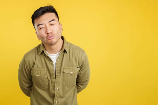 Chinese young man kissing with eyes closed in studio with yellow background