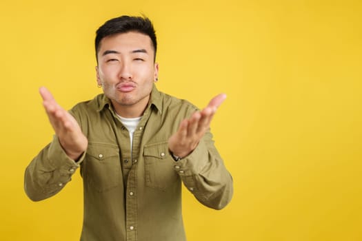 Chinese man blowing a kiss while looking at the camera in studio with yellow background