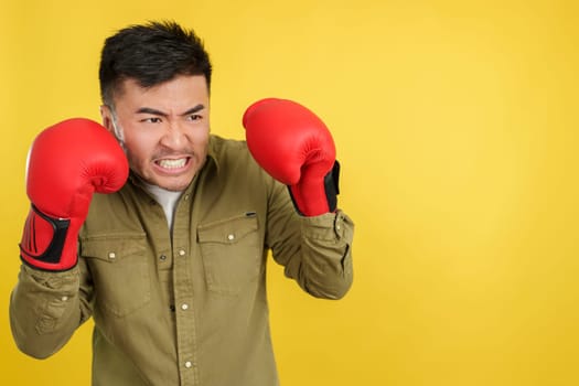 Angry chinese man with boxing gloves with fighting pose in studio with yellow background