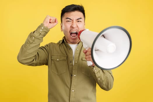 Angry chinese man shouting and looking at camera using a loudspeaker in studio with yellow background