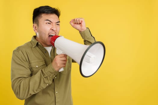 Upset chinese man shouting using a loudspeaker in studio with yellow background