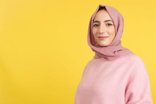 Happy muslim woman wearing hijab looking at the camera in studio with yellow background
