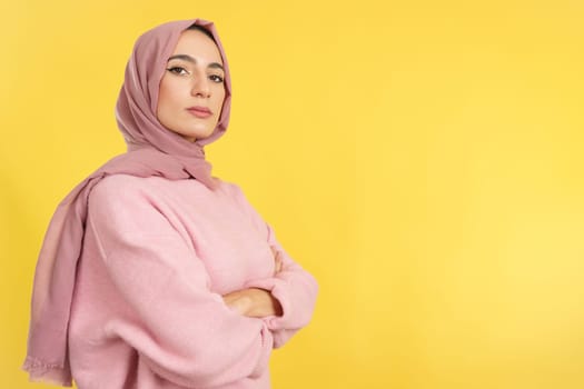 Strong and proud muslim woman standing looking at camera in studio with yellow background