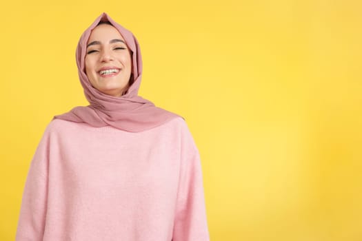 Beauty young muslim woman wearing hijab smiling in studio with yellow background
