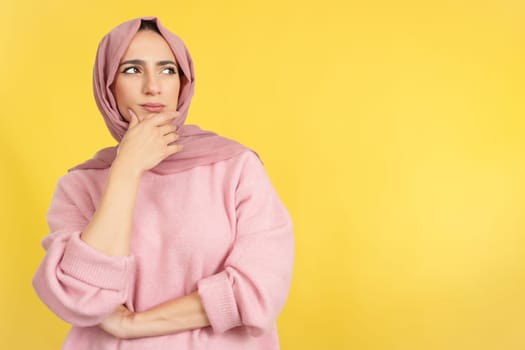 Muslim woman with hand on face and thoughtful expression in studio with yellow background