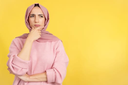 Worried muslim woman looking away with pensive expression in studio with yellow background