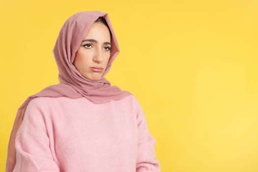 Sad muslim woman wearing head scarf looking away in studio with yellow background