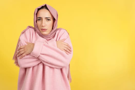 Muslim woman looking at camera in the cold in studio with yellow background