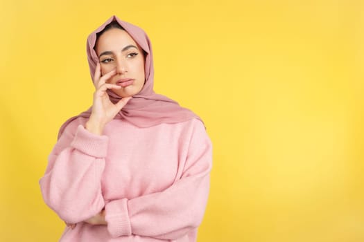 Bored muslim woman standing and looking away in studio with yellow background