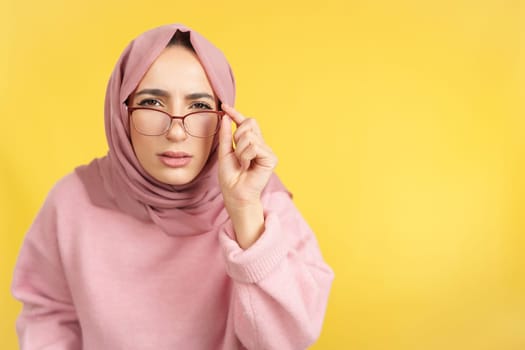 Muslim woman taking off her glasses to see in studio with yellow background