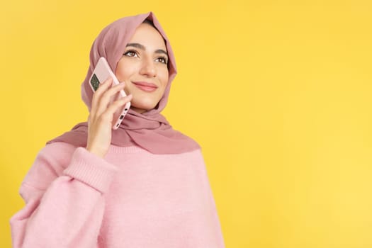 Beauty happy muslim woman talking to the mobile in studio with yellow background