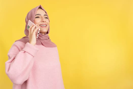 Happy muslim woman talking to the mobile phone in studio with yellow background