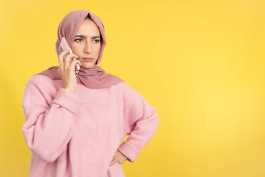 Angry muslim woman talking to the mobile in studio with yellow background