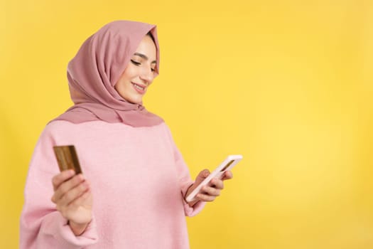 Muslim woman using the mobile and card to shopping online in studio with yellow background