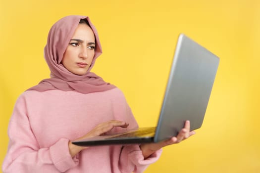 Worried muslim woman with a problem with a laptop in studio with yellow background