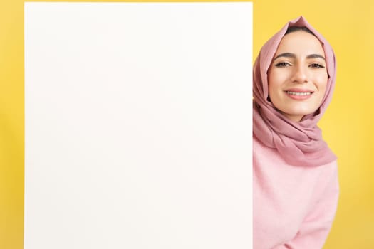Happy muslim woman holding a blank panel in studio with yellow background