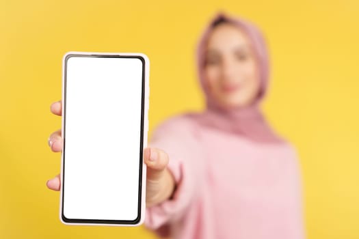 Blank screen of the mobile held by a muslim woman in studio with yellow background