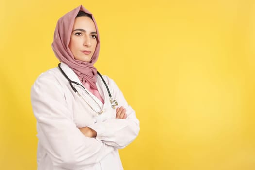 Serious female muslim doctor with arms crossed looking away in studio with yellow background