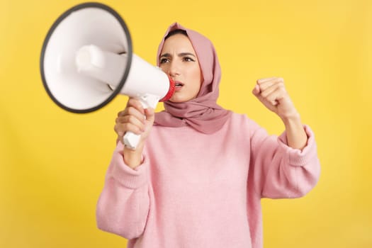 Upset muslim woman using a loudspeaker in anger in studio with yellow background